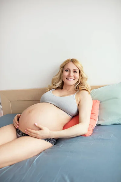 一个漂亮的孕妇在卧室里笑着躺在床上的画像 — 图库照片