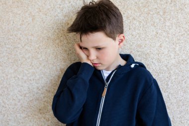 Duvara dayanmış 10 yaşındaki üzgün bir çocuğun portresi.