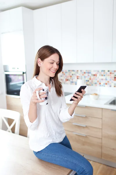 Молодая женщина, использующая мобильный телефон на кухне — стоковое фото