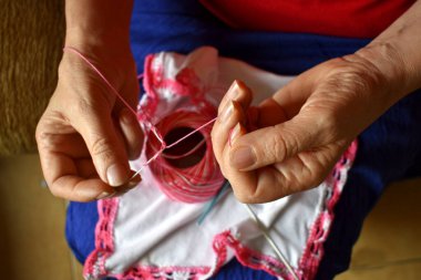 Yaşlı kadın işlemesini pembe beyaz bir iplik ve birkaç iğneyle yapıyor.