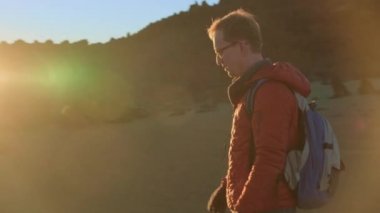 Yüksek bir dağ yolunda, batan güneşin ışınlarında bir yürüyüşçü.