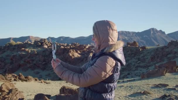 Mooi meisje vlogger neemt selfies tegen een marsmannetje landschap in koud en winderig weer — Stockvideo