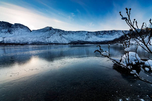 Solar halo in the mountains near a lake covered with ice on a winter evening