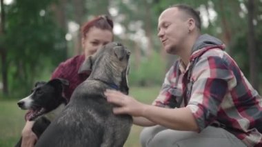 Gülümseyen adamın köpeği okşaması ve arka planda oturan bulanık kadın ve evcil hayvan gibi evcil hayvanla konuşması. # Mutlu çift yaz ormanlarında #.