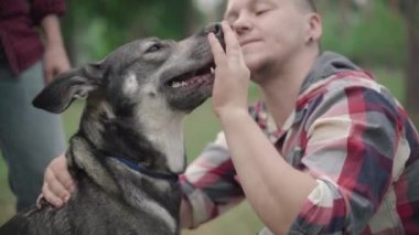 Açık havada evcil köpeğin kafasını okşayan bulanık adamın yakın çekimi. Mutlu gülen evcil hayvan sahibi ormandaki ya da parktaki evcil hayvanla eğleniyor..