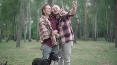 Sabahları gülen bir kadınla konuşan olumlu bir adam. Köpeğiyle birlikte yaz ormanında duruyor. Kafkasyalı mutlu bir ailenin portresi açık havada evcil hayvanlarla yürümekten zevk alıyor..