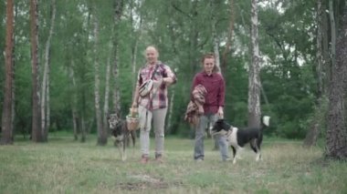 Beyaz bir çiftin yaz ormanlarında ya da parkta köpeklerle piknik yaparken geniş açılı portresi. Evcil hayvanlarıyla gülümseyen adam ve kadın sepet ve battaniyeyle dışarıda dolaşıyorlar..