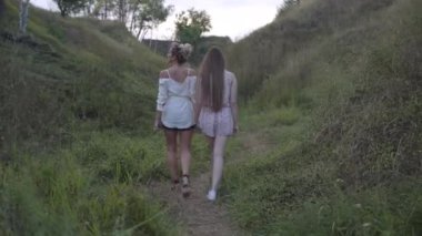 Bulutlu bir günde açık havada el ele tutuşan iki beyaz kadının geniş açılı görüntüsü. Kaygısız, kendinden emin anne ve yetişkin kızı sonbaharda doğal parkta geziniyor..