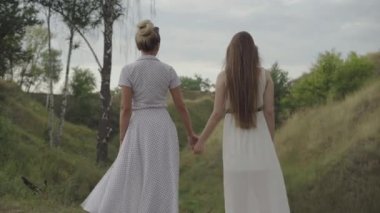 Kendine güvenen ince anne ve kızın el ele tutuşup birbirlerine baktıkları arka manzara. Genç ve yetişkin Kafkasyalı kadınlar hafta sonları açık havada rüzgarlı bir gün geçiriyorlar..