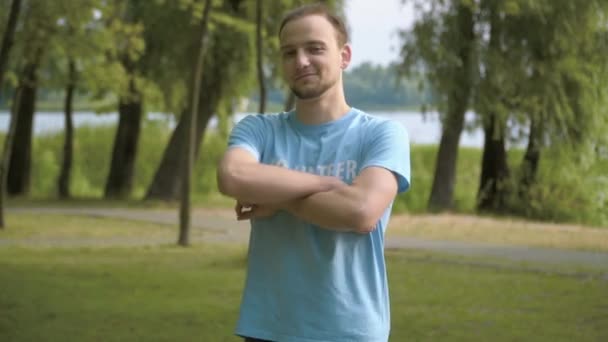 Retrato de jovem confiante voluntário do sexo masculino cruzando as mãos e sorrindo para a câmera. Bonito homem caucasiano posando em parque de verão claro após a limpeza. Protecção do ambiente e ecologia. — Vídeo de Stock