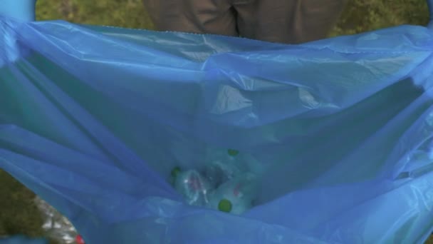 Крупним планом мішок зі сміття з руками в рукавичках кидає сміття всередину. Невпізнаваний доброволець виїжджає зі сміттям, зібраним у літньому парку на відкритому повітрі. Забруднення навколишнього середовища та захист . — стокове відео