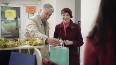 Kafkasyalı mutlu bir çiftin Noel 'de hediye alırken portresi. Gülümseyen adam ve kadın kasada satıcıyla konuşuyor ve alışveriş torbalarını alıyorlar. Kara Cuma ve tüketim kavramı.