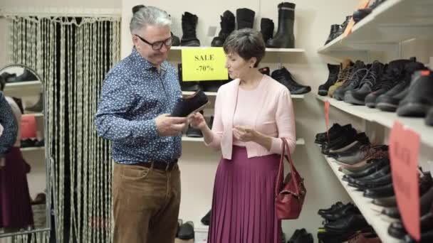 La coppia più anziana caucasica sicura che sceglie scarpe in negozio durante venerdì nero. Ritratto di uomo e donna serio che parlano e guardano le calzature durante le vendite. Shopping e consumismo. — Video Stock