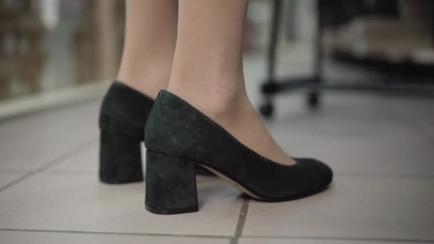 Розміщення жіночих кавказьких ніг на чорних високих підборах. Невпізнавана жінка, яка приміряє взуття в магазині. Покупка і концепція моди. — стокове відео