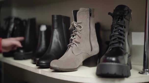 Row of winter shoes standing on shelf with young female Caucasian hand touching and picking on boot. Unrecognizable woman choosing shoes in shop. Black friday sales concept. — Stock Video