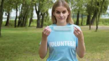 Kendinden emin kadın gönüllü Covid-19 yüz maskesi takıyor yaz parkında ve kameraya bakıyor. Açık havada ekolojiyle ilgilenen beyaz bir kadının portresi. Çevre koruma.