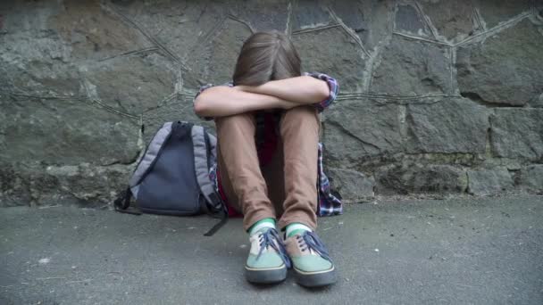 Retrato de estudante caucasiano chateado sentado contra a parede de pedra e chorando. Menino morena intimidada passar férias escolares na solidão. Conceito de depressão e bullying. — Vídeo de Stock