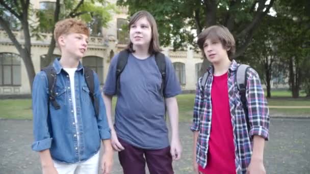 Pozitivní bělošští spolužáci stojící venku po studiu a rozhovoru. Portrét tří školáků, jak si po vyučování povídají na školním dvoře. Vzdělání a přátelství. — Stock video