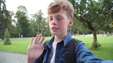Açık havada video blogu kaydetmek için el sallayan ve konuşan pozitif kızıl saçlı öğrencinin yakın çekimi. Kafkas çocuk blogunun mutlu portresi. Z neslinin modern yaşam tarzı.