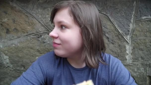 Close-up of plump brunette schoolboy looking around and biting sandwich. Potret anak gemuk bertubuh gemuk Kaukasia bersembunyi dengan makanan ringan di luar. Tidak sehat makan dan junk food konsep. — Stok Video