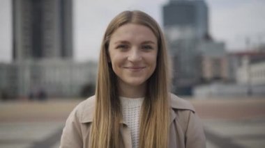 Şehir merkezinde bulutlu bir günde kameraya gülümseyen güzel beyaz kadın portresi. Bulutlu bir sonbahar ya da bahar gününde poz veren neşeli, pozitif bir bayan..