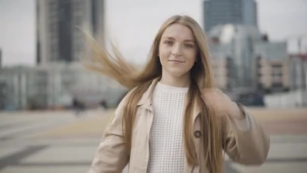 Portrait de charmante jeune femme aux longs cheveux raides tournant sur la place de la ville. Belle dame caucasienne posant à l'extérieur par temps nuageux et souriant à la caméra. Beauté et mode de vie. — Video