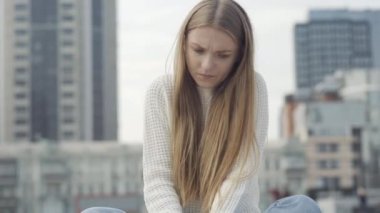 Ateşi olan üzgün genç bir kadın alnına ve yüzüne dokunuyor ve iç çekiyor. Şehir meydanında oturan hasta beyaz kadının portresi. Tıbbi konsept.