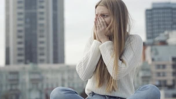 Mulher jovem doente tosse como sentado na praça urbana da cidade no dia nublado da primavera ou do outono. Retrato de senhora caucasiana doente com sintomas ou doença respiratória ao ar livre. — Vídeo de Stock