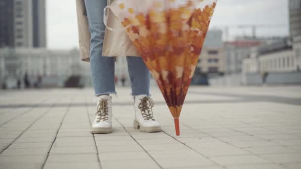 Onherkenbare jonge vrouw die op het stadsplein staat met gesloten paraplu en draaiende accessoire. zorgeloze blanke dame wacht buiten op regenachtige bewolking lente of herfst dag. — Stockvideo