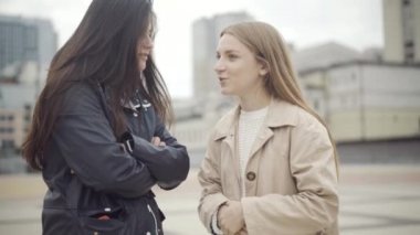 Açık havada dedikodu yapan iki güzel kadının portresi. Şehir meydanında durmuş konuşan beyaz, çekici bayan arkadaşlar. Arkadaşlık ve dedikodu kavramı.