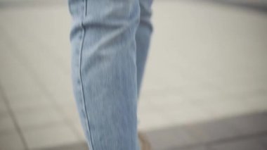 Kamera, şehir meydanında dikilip kameraya gülümseyen günlük kot pantolon ve beyaz kazak giyen ince beyaz kadın boyunca hareket ediyor. Açık havada poz veren güzel genç bir bayan portresi..