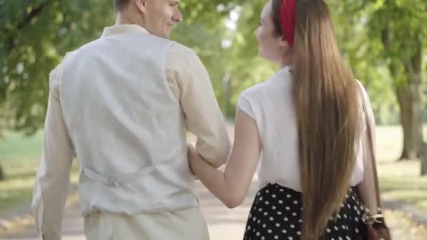 Вид сзади влюбленной романтичной молодой пары, прогуливающейся в солнечном парке и разговаривающей. Красивый белый мужчина и красивая женщина встречаются на открытом воздухе в летний день. Любовь и романтика. — стоковое видео