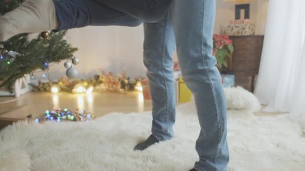 Homme méconnaissable filant avec une femme la veille du Nouvel An avec arbre de Noël décoré à l'intérieur. Jambes masculines et féminines de personnes qui s'amusent à la maison la veille des vacances. — Video