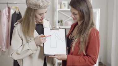 Pozitif odaklı genç moda tasarımcısı atölyedeki terziye ya da terziye elbise taslağını açıklıyor. İçeride tasarımı tartışan iki güzel beyaz kadının portresi. Meslek kavramı.