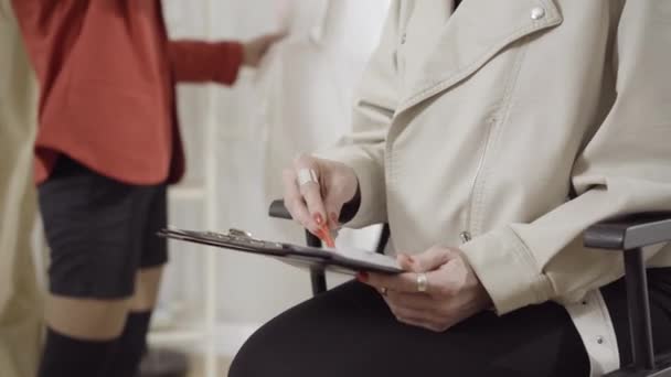 Unrecognizable designer drawing garment sketch in atelier with tailor or seamstress hanging clothes at the background. Young creative Caucasian woman designing in atelier. Fashion and creativity. — Stock Video