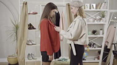 Tarz sahibi, güler yüzlü, beyaz bir kadının içeride arkadaşının ceketini incelemesi. Atölyede kıyafet seçen pozitif genç bayanlar. Kendine güvenen moda tasarımcıları koleksiyon eğilimlerini tartışıyor.