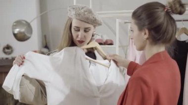 Moda tasarımcısı terzisinin yardımıyla atölyeden kıyafet seçen kendine güvenen şık müşterinin portresi. Beyaz bluzu inceleyen ve konuşan zengin beyaz kadın..