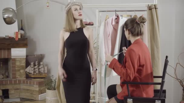 Side visning af unge professionelle syerske dressmaker tager målinger af elegante kunder hånd i atelier. Selvsikker hvid skrædder designer ved hjælp af målebånd til design. – Stock-video