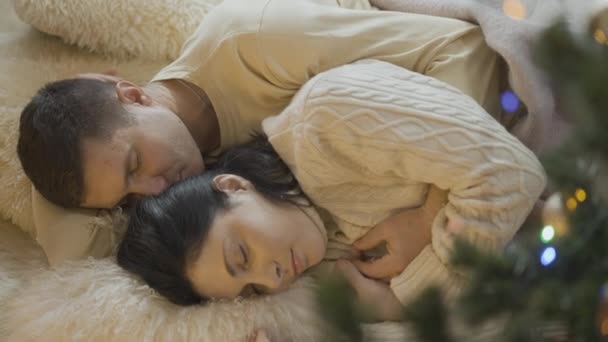 Blick aus der Vogelperspektive auf ein glückliches Paar, das am Silvesterbaum zu Hause schläft. Porträt eines entspannten kaukasischen Paares an Heiligabend im Haus. Entspannung in der Ferienzeit. — Stockvideo