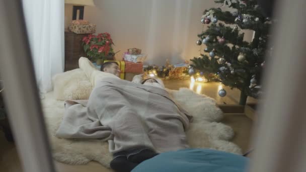 Reflexão no espelho de casal feliz relaxado acordar na manhã de Natal em casa. Homem e mulher caucasiano alegre deitado na árvore de Ano Novo dentro de casa sorrindo e falando. Conceito de felicidade. — Vídeo de Stock