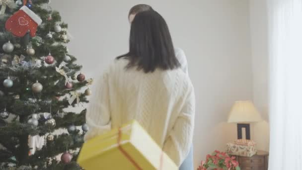 Pohled na radostnou šťastnou ženu, jak dává vánoční dárek manželovi a líbá vzrušeného bělocha. Milující žena dělá překvapení na Nový rok pro rozkošného partnera. — Stock video