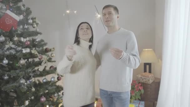 Средний снимок радостной кавказской пары с искрами, наслаждающейся рождественским праздником дома. Счастливый муж и жена или парень и девушка празднуют Новый год в помещении. — стоковое видео