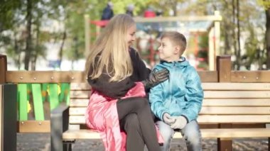 Neşeli bir kadın ve oğlanın gülümseyen baş parmaklarını kaldırıp güneş ışığında kameraya baktıkları portresi. Mutlu Kafkas anne ve oğlu arka planda bulanık oyun parkı ile sonbahar parkında poz veriyor..