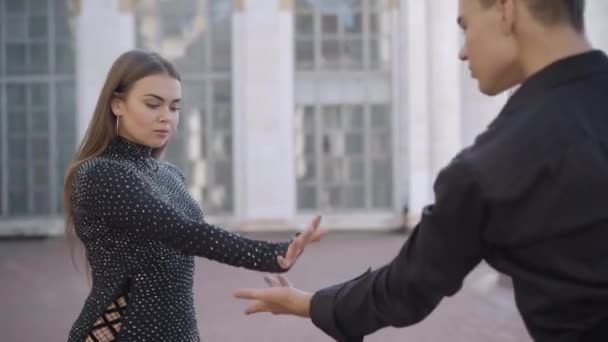 Självsäkra par dansare börjar uppträda i urban stad på solig dag. Ung vit man och kvinna som håller händer dansar i solstrålar med byggnad med kolumner i bakgrunden. — Stockvideo