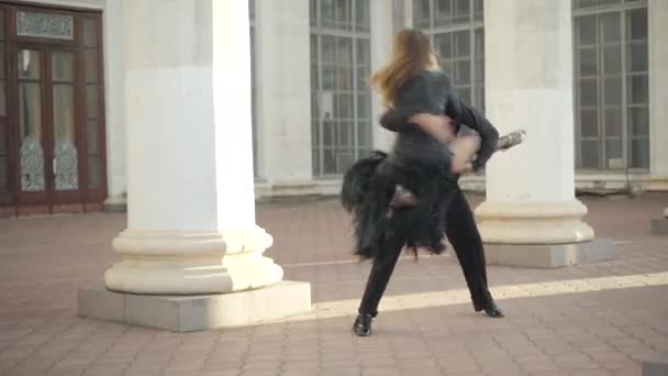 Szerokie ujęcie mężczyzn łapiących i zginających szczupłą kobietę między miejskimi kolumnami. Portret zawodowych baletnic kaukaskich wykonujących na świeżym powietrzu w słoneczny dzień. — Wideo stockowe