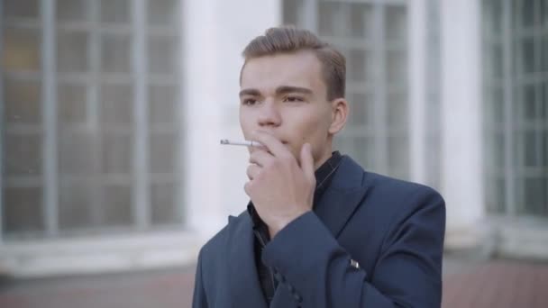 Şehir caddesinde sigara içen yakışıklı esmer adamın portresi. Açık havada duran düşünceli, beyaz bir adam. Tütün bağımlılığı konsepti. — Stok video
