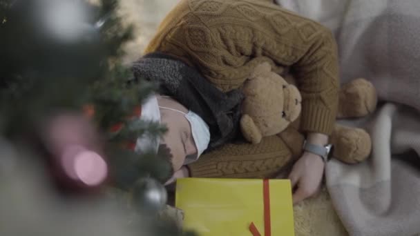 Hoge hoek van de jonge man in Covid gezichtsmasker slapen knuffelende teddybeer op oudejaarsavond. Ontspannen zorgeloze blanke man op kerstochtend thuis op coronavirus pandemie. — Stockvideo