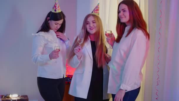 Drie zelfverzekerde jonge duizendjarige vrouwen met champagneglazen op verjaardagsfeestroddels. Portret van mooie blanke vrienden die geruchten binnen delen. Vrouwelijkheid en vriendschap. — Stockvideo