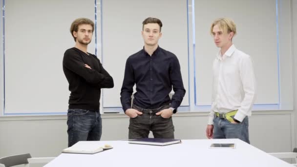 Szerokie ujęcie portretu trzech młodych, pewnych siebie białych mężczyzn stojących w biurze i patrzących przed kamerą. Udane millenium współpracowników pozowanie w sali konferencyjnej w pomieszczeniach. Sukces i koncepcja biznesu. — Wideo stockowe