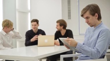 Ofisteki tablette internette gezinen kafası karışık genç bir beyaz adam arka planda konuşuyordu. İçerideki girişimi analiz eden konsantre milenyum çalışanının yan görünüm portresi.